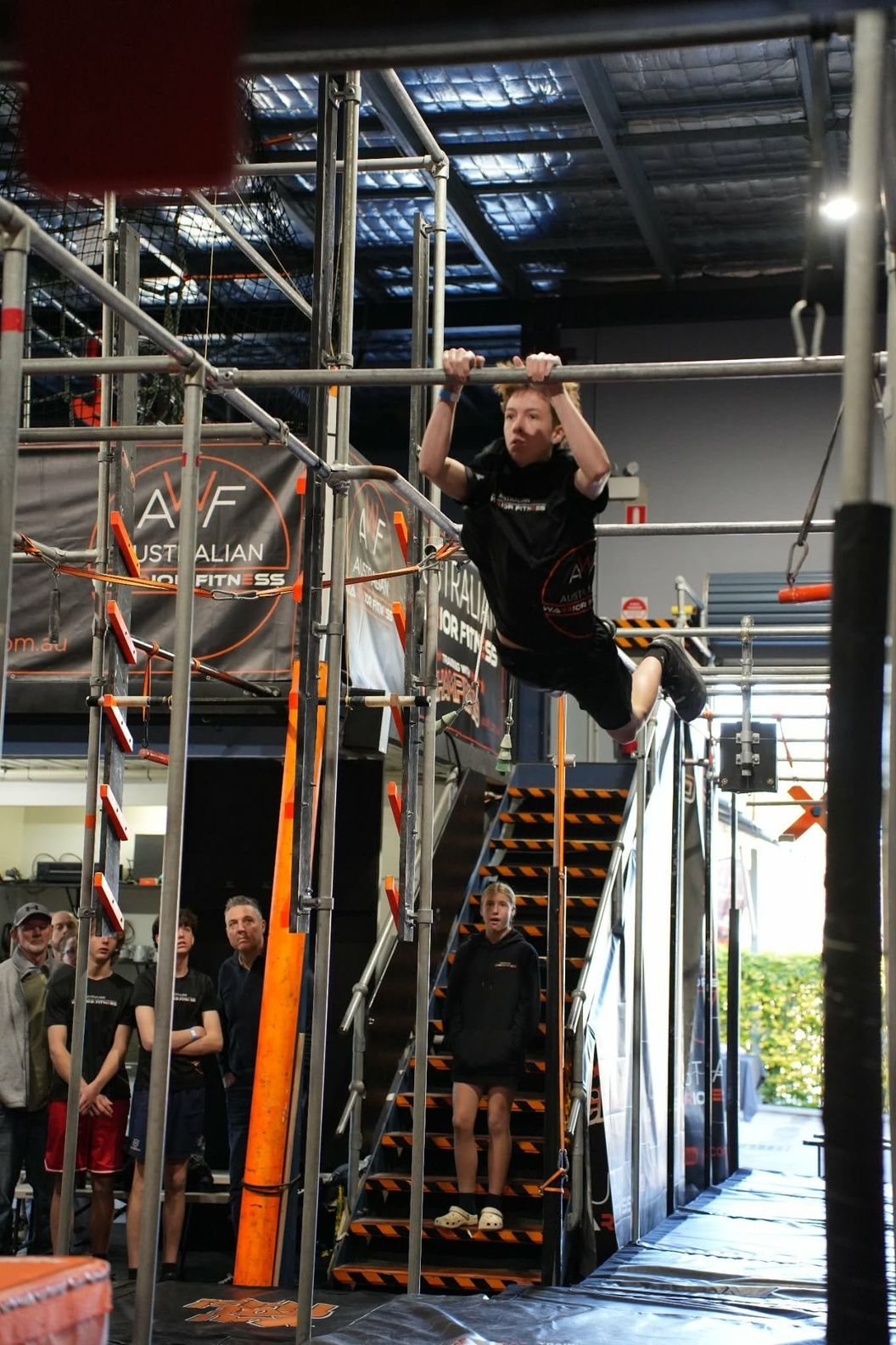 Ninja athlete swinging between bars high on the AWF rig as spectators watch below
