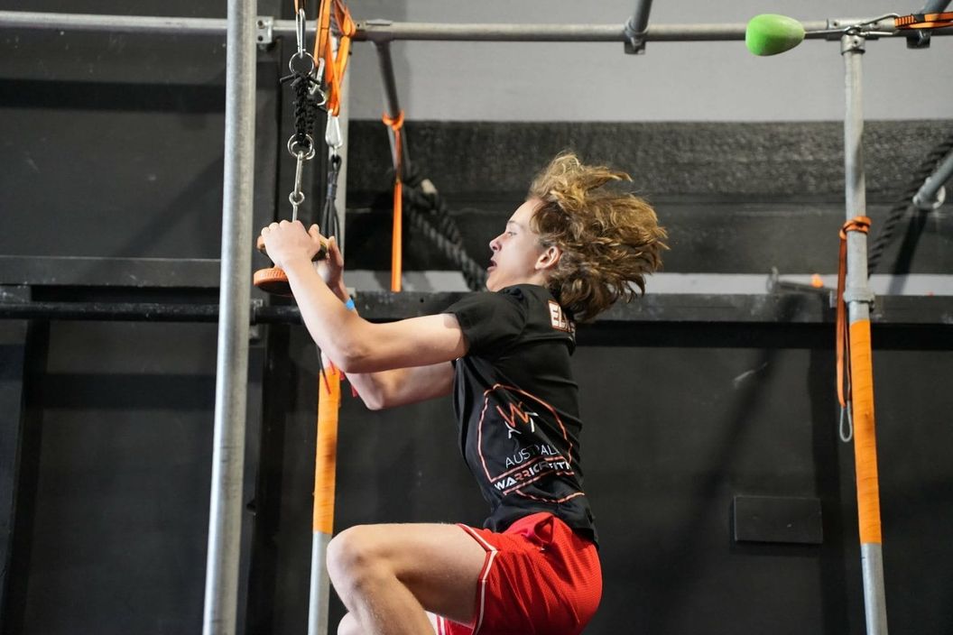 Young ninja gripping a hanging rope obstacle on the AWF rig in Gosford