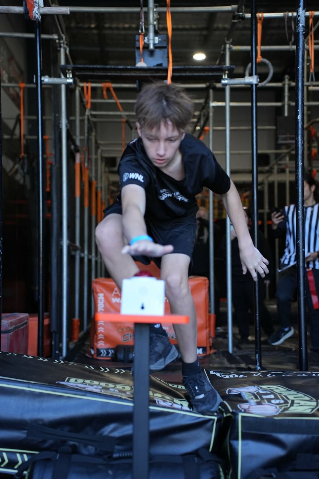 Boy balancing on a small step obstacle in front of the AWF ninja rig