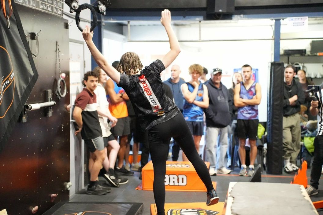 Competitor reaching for a hanging ring while a crowd watches at AWF