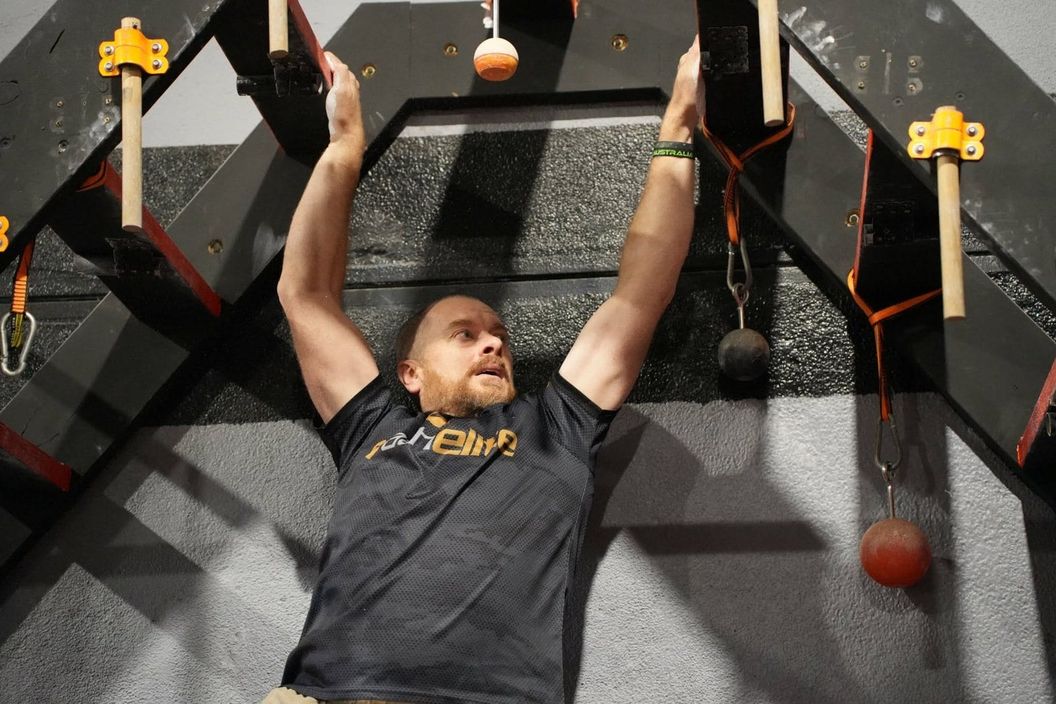 Adult ninja hanging from grip pegs on the AWF hang wall
