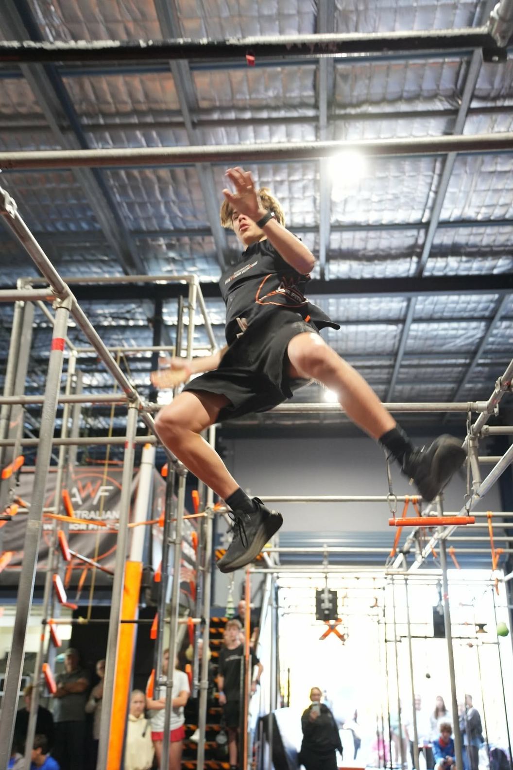 Athlete swinging through the air on the AWF ninja rig under the gym lights