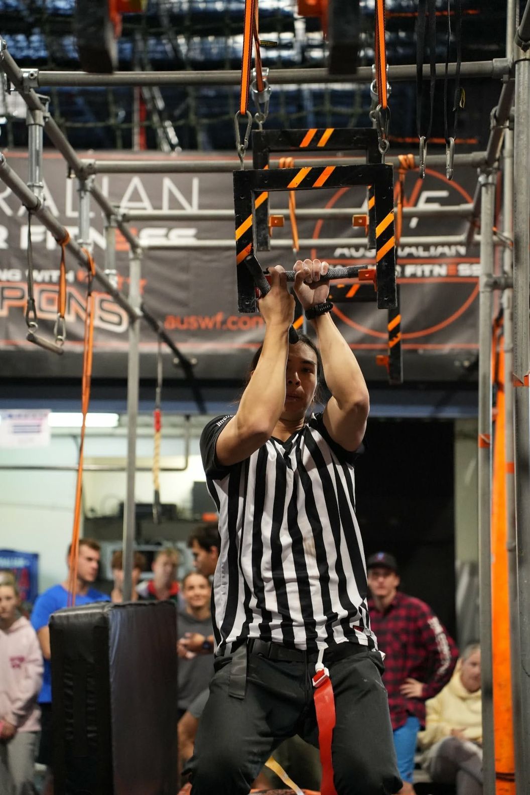 Referee in a striped shirt testing a hanging handle obstacle at AWF
