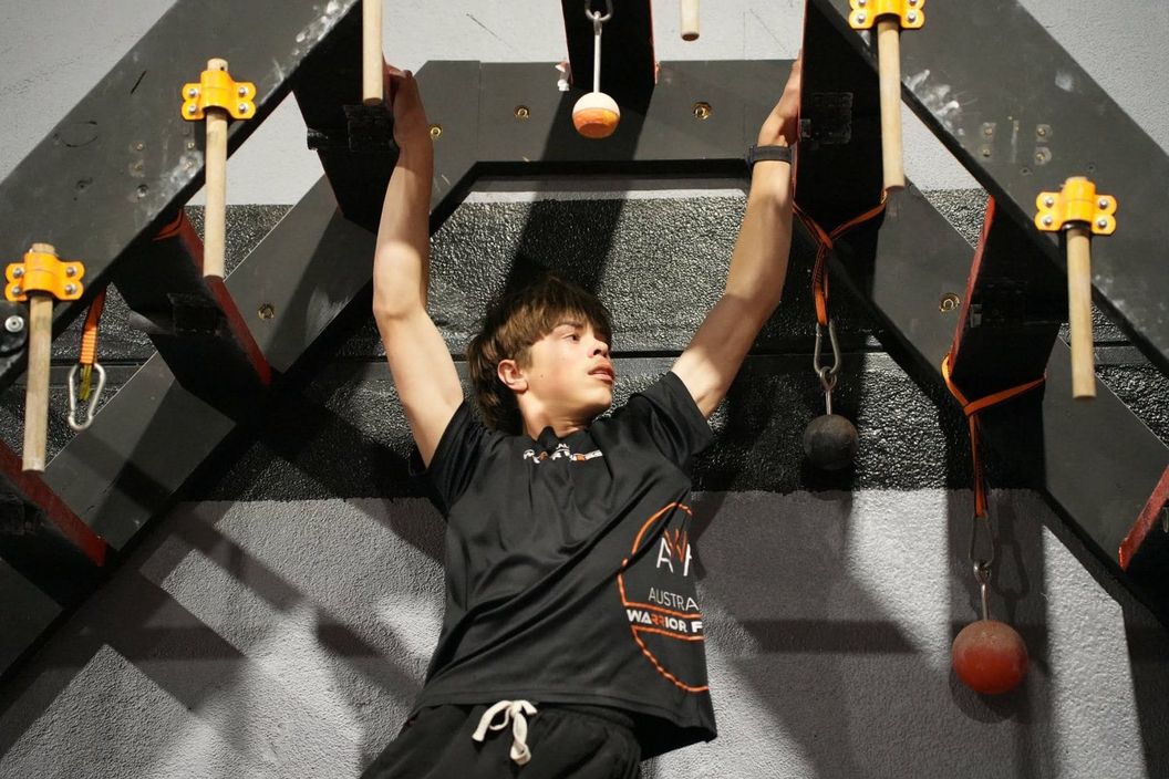Teen ninja hanging from grip pegs on the AWF hang wall