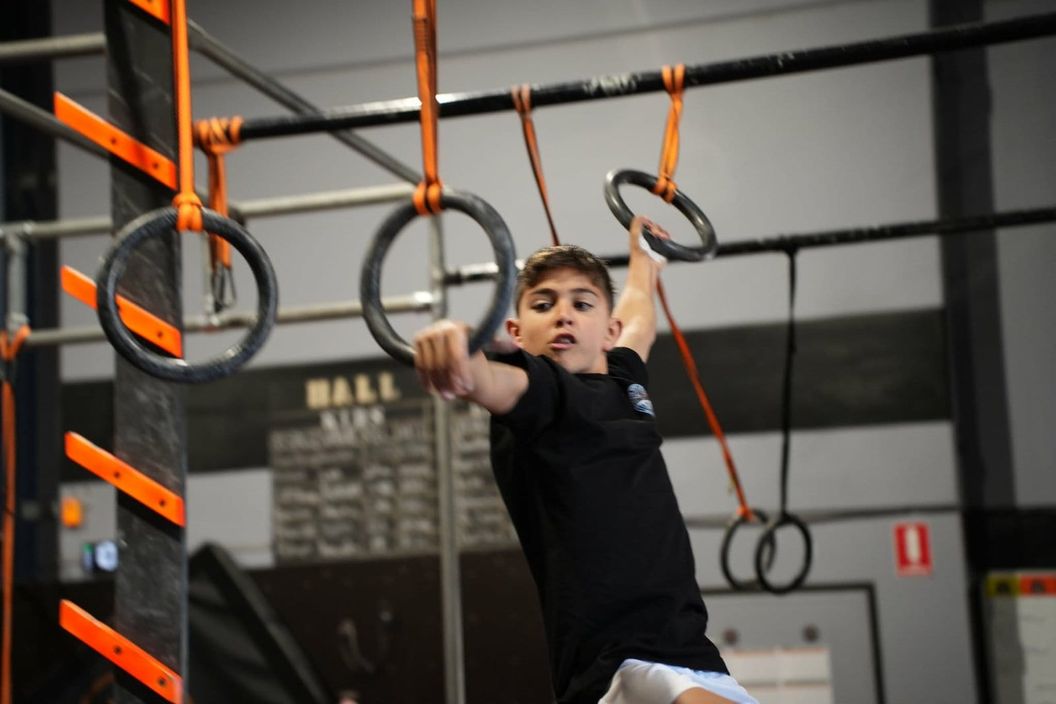 Smiling boy swinging across the hanging rings at AWF Gosford